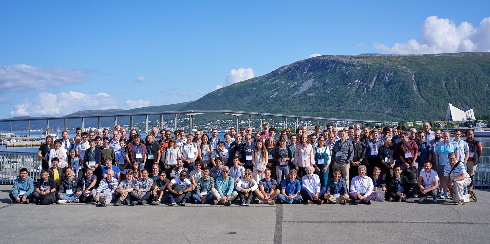 Group photo of the ISSAC 2023 participants on the Tromsø waterfront, with the Tromsø bridge and the Arctic Cathedral behind